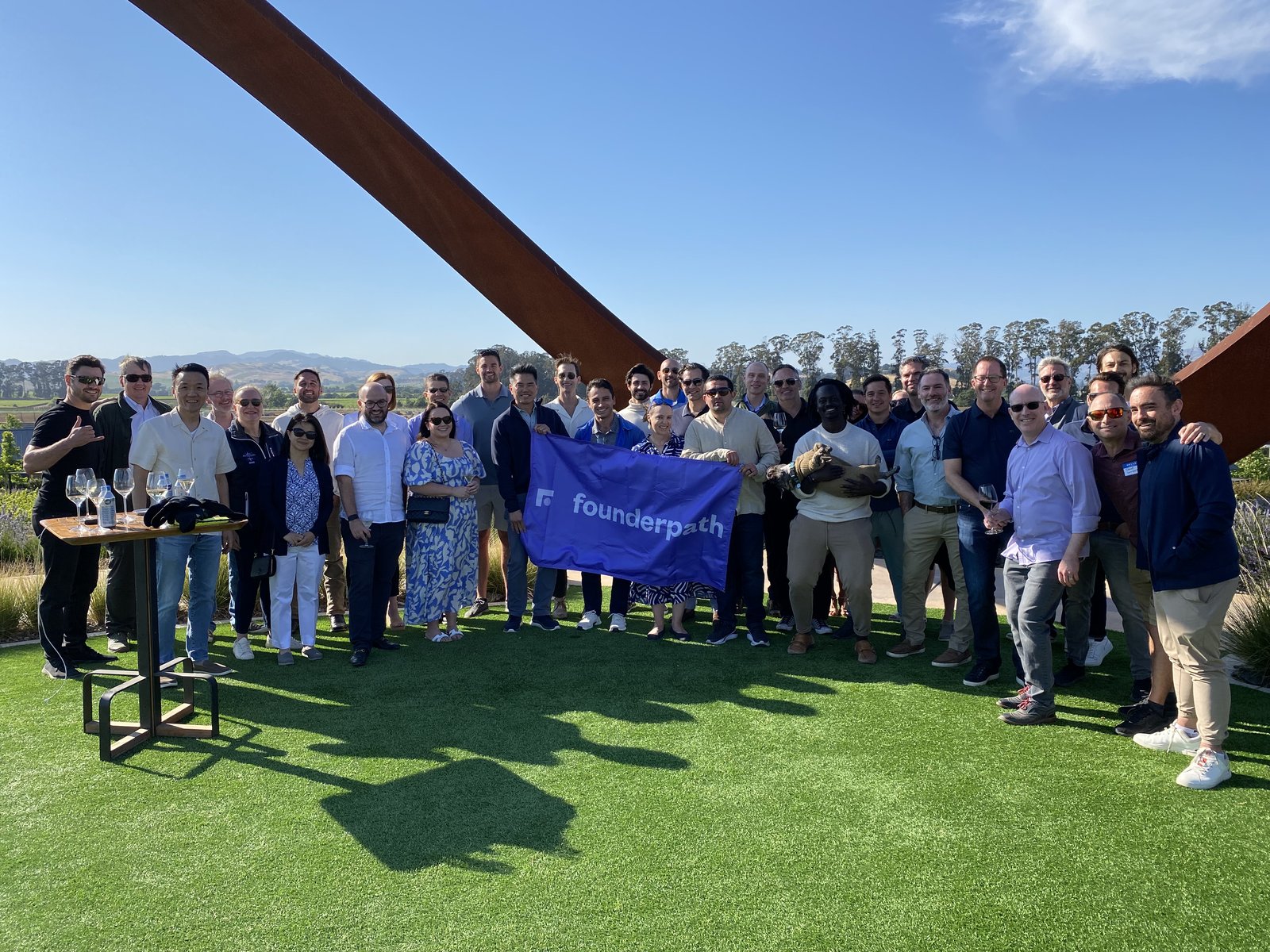 The full group of founders with the Founderpath flag beneath the vineyard arches